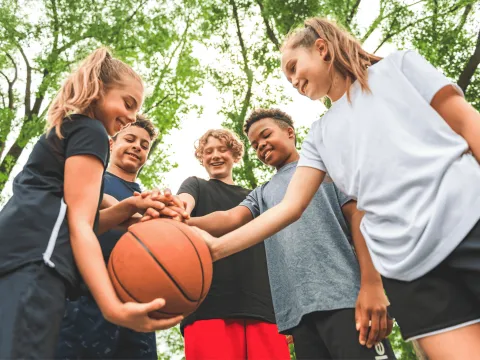 Five Teens Huddle Around a Basketball in a Park