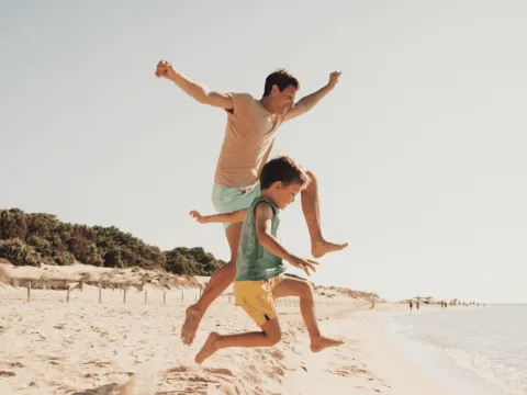 A Father and Son Jump Off a Dune on the Beach