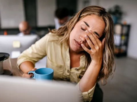 A Woman Presses Her Fingers to the Bridge of Her Nose While Drinking a Cup of Coffee at Home