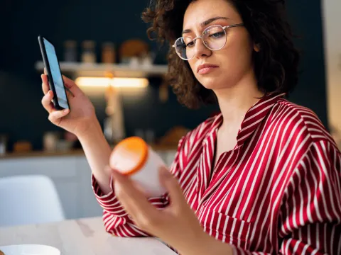 A Woman Looks at a Bottle While Researching it on Her Phone.