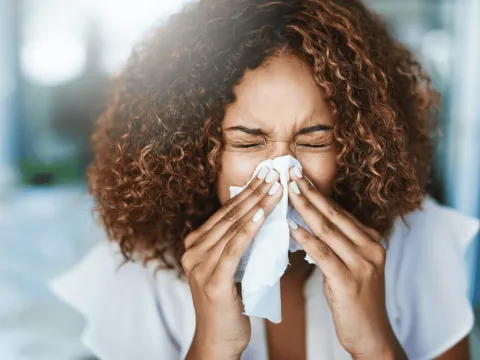A Woman Sneezes into a Tissue at Home