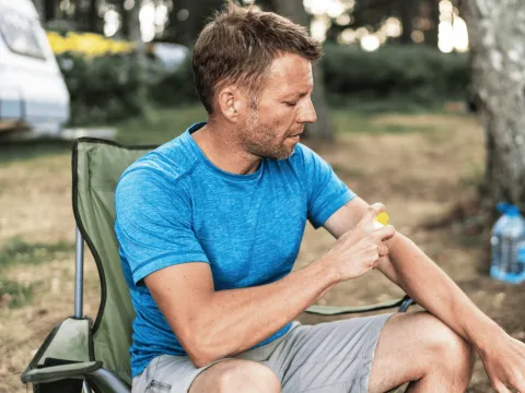 A Man Scratches His Arm While Camping in a Park