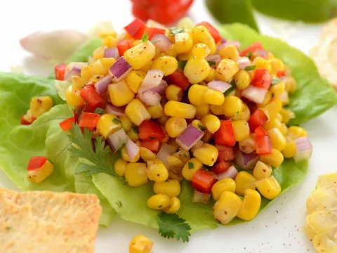 Corn with diced red pepper and red onion salsa on a bed of lettuce