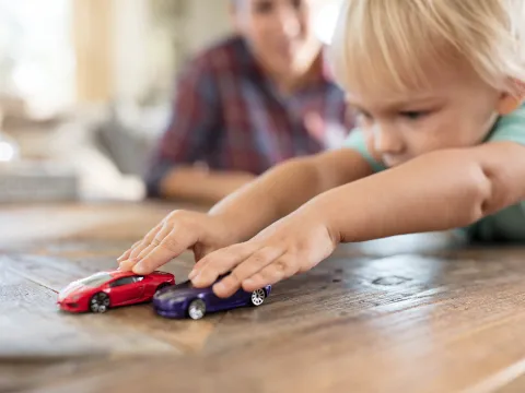 Little Boy Playing with Cars with Father in Background 