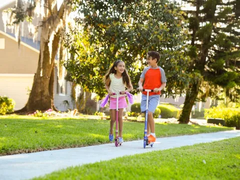 A brother and sister ride scooters outside