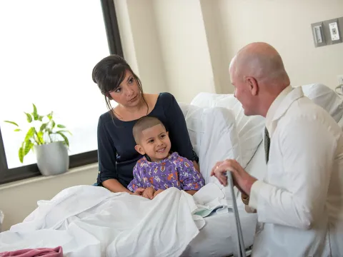 A child patient sits with his mom and smiles at his doctor.
