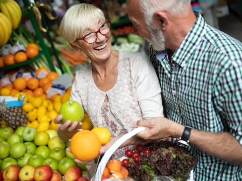 A senior couples shopping for produce with a basket.