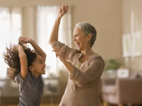 An elementary-aged girl and an older female relative dancing and smiling indoors