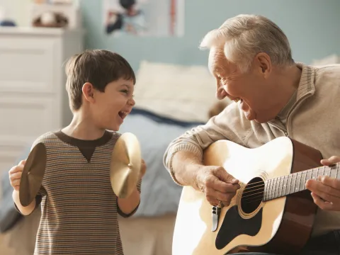 Grandfather playing guitar for grandson while grandson plays the cymbals