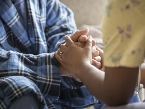 Close-up of a nurse and cancer patient holding hands.
