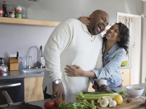 A couple shares a sweet moment as they prepare vegetables in their kitchen