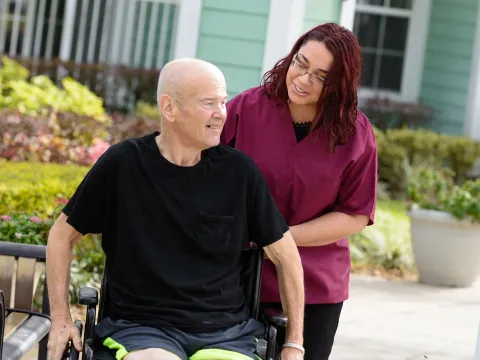 Elderly man in a wheelchair outside with a nurse.