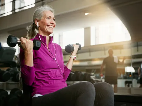An elderly woman lifting weights at the gym.
