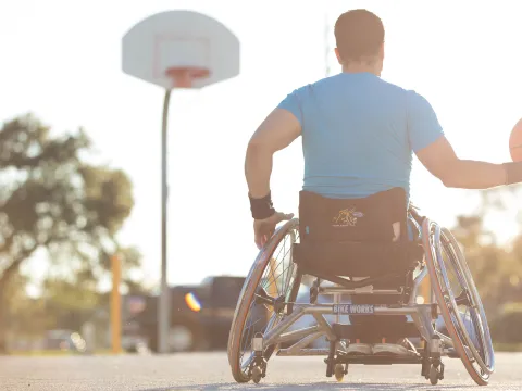 Man in a wheelchair playing basketball outside.