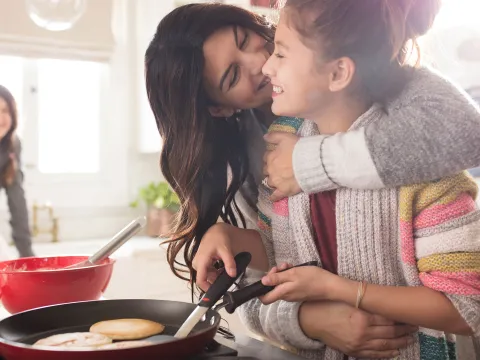 A woman hugging her daughter in the kitchen.