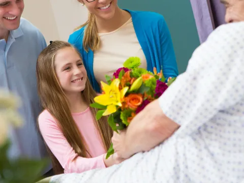 Family with child giving flowers to a hospital patient