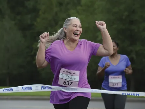 An older woman is ecstatic as she crosses the finish line of a charity foot race