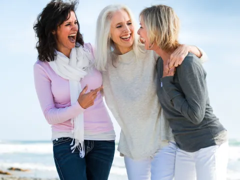Three women laughing during a walk on the beach.
