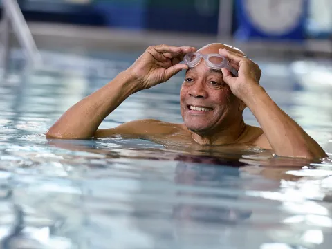 An older man puts on his goggles in an indoor exercise pool