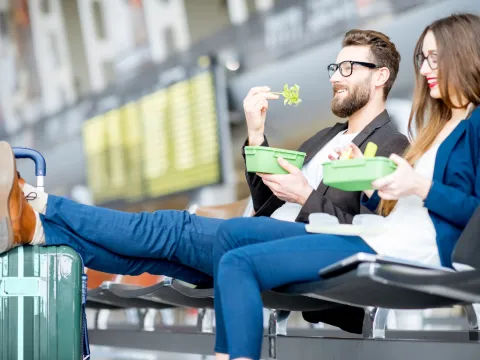 A young couple sitting in the airport lounge, eating healthy meals.