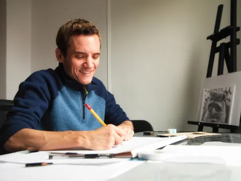 A man drawing with a pencil at a desk.