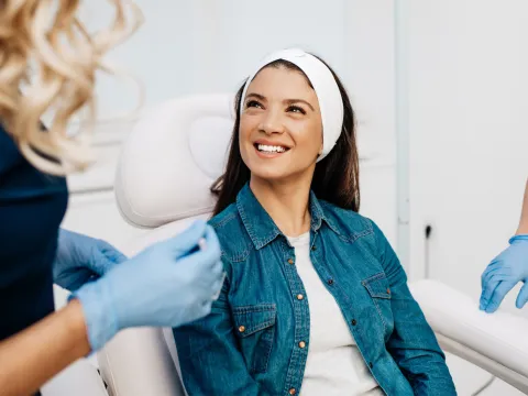 A woman smiles at her healthcare provider before getting a facial treatment.