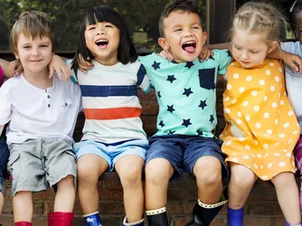 A happy group of children sit on a bench outdoors. 