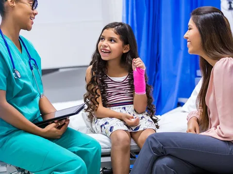 Child with a cast on her arm is sitting with a doctor and her mother