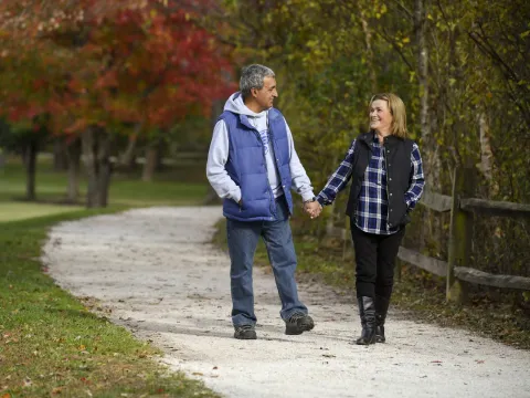 Couple walking down a path outdoors in the fall holding hands.