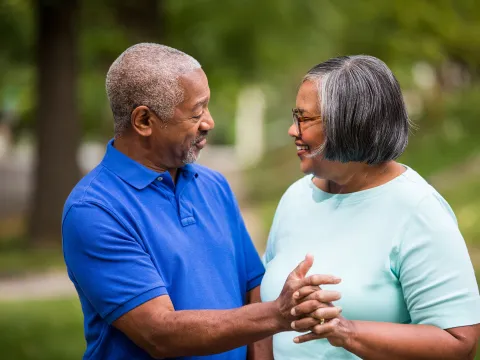 An elderly couple, enjoying each other company while grabbing hands in the park.
