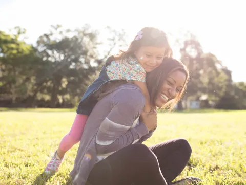 Daughter climbing on mom outdoors