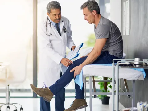 Doctor checking a male patient's knee.