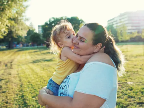 Woman standing in a field holding her child.