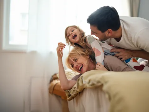 A mother and father play with their child in a bedroom.