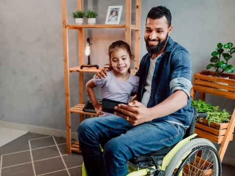 A father in a wheelchair taking a selfie photo with his young daughter.