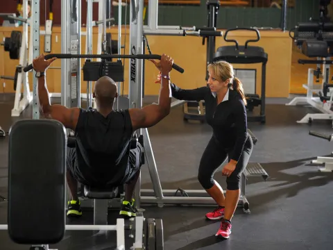 Female personal trainer coaching male trainee with a lat pulldown exercise.