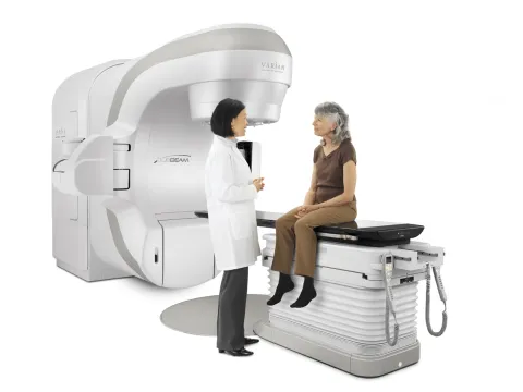 Oncologist with a female patient sitting on the bed of the TrueBeam Radiotherapy System from Varian Medical Systems.