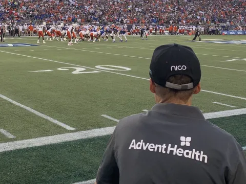 Man wearing shirt with AdventHealth logo on the sidelines of a football game.
