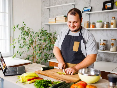 A man cutting up vegetables in his kitchen.