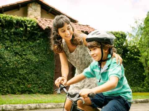 A mother helps her child learn to ride a bike.