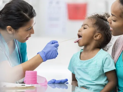 Little girl sitting on her mother's lap sticking her tongue out for the doctor.