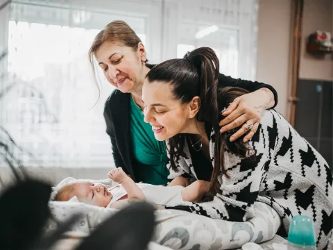 Grandmother and mother smiling at a baby laying on a bed.
