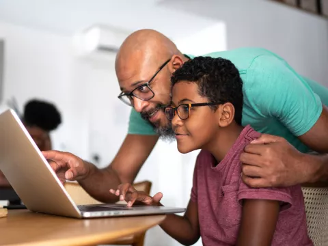 A father and son look at a laptop together.