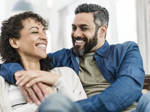 A couple laughing together on their couch at home.