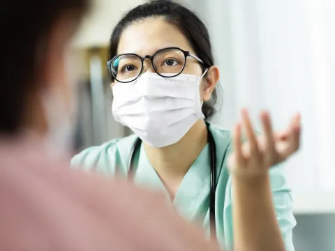 A doctor wearing a mask speaks with a patient.