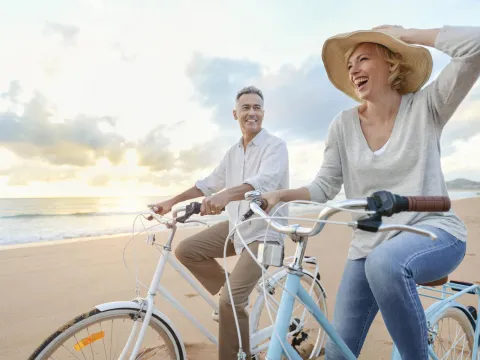 Man and woman in a hat riding bicycles on the beach at sunset.