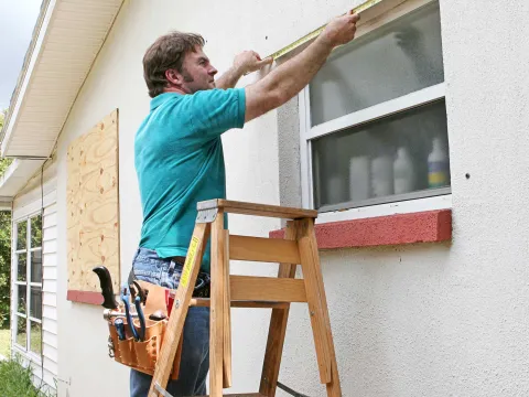 A journeyman measuring a window of a house