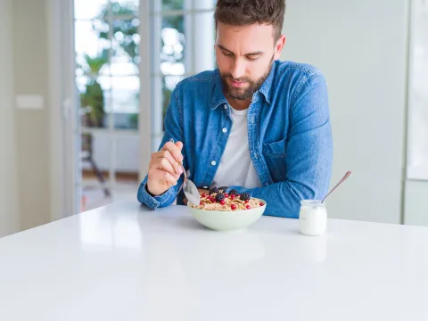 A gentleman eating a bowl of cereal with berries and a cup of yogurt