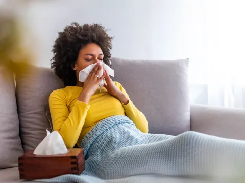 A woman sneezes on her couch at home