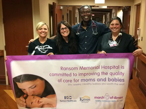 Physician and nurses holding a banner of the work they do for mothers and babies.